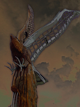 A wooden eagle statue with a metallic wing and talons stands against a strange, dark sky.