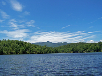 A beautiful view of Price Lake along the Blue Ridge Parkway with Grandfather Mountain rising in the distance against a blue sky.